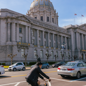Image of cyclist passing parked cars in front of SF City Hall