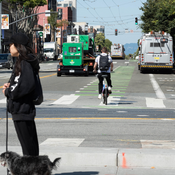 Image of a pedestrian, cyclist, buses, and cars on a busy street in San Francisco