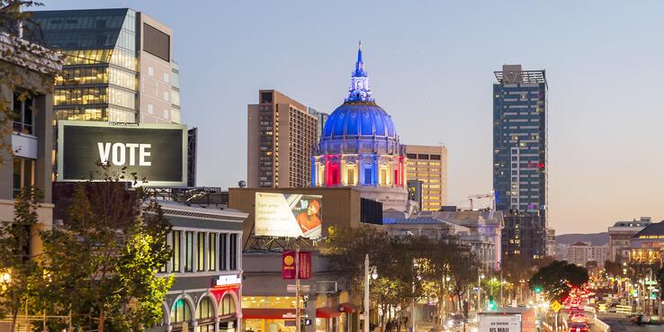 photo of San Francisco City Hall lit up in red white and blue and billboard that says "Vote"