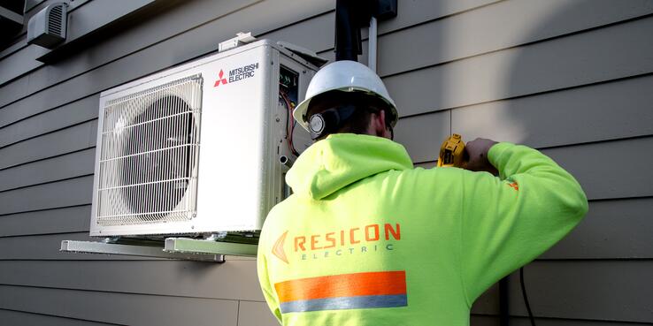 Construction worker, Doug Berger, helps install energy efficient heat pumps outside resident homes.